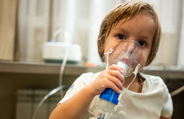 small kid receiving asthma treatment and using inhaler at home.