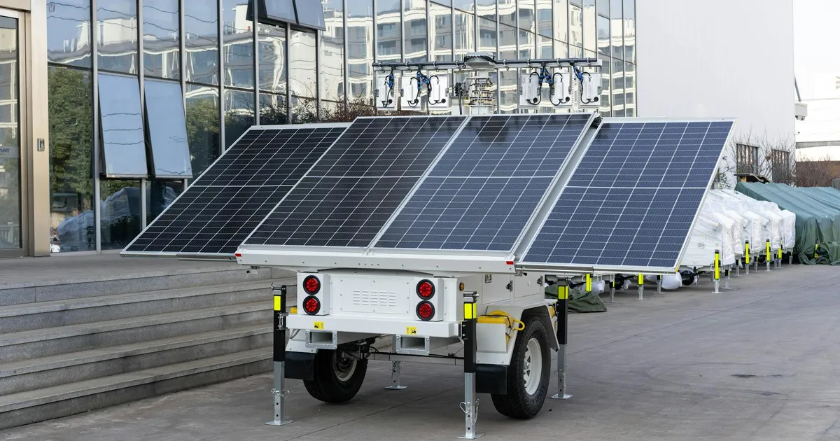 A mobile solar panel trailer parked outdoors by a modern building, showcasing renewable energy technology.