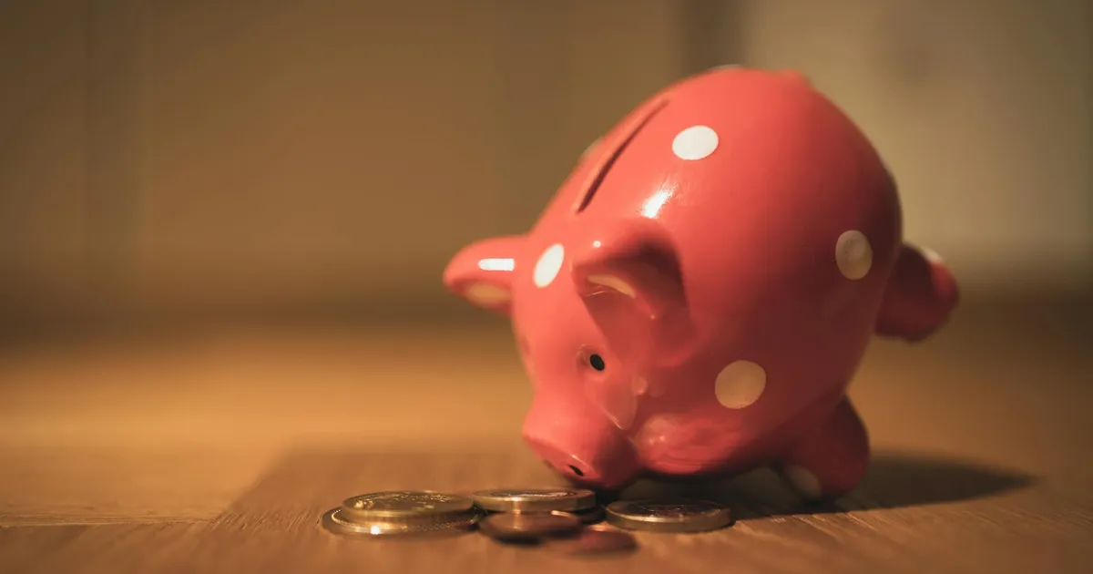 A red ceramic piggy bank with polka dots surrounded by coins, symbolizing savings and finance.