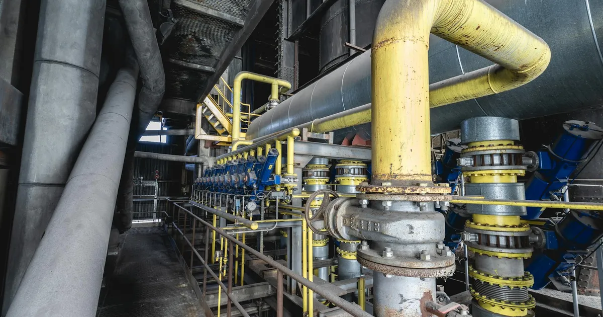 Close-up of an intricate industrial pipeline system featuring yellow valves and steel structures inside a factory.