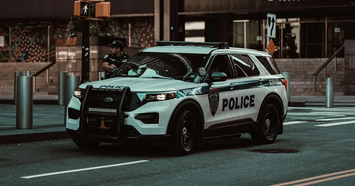 A police car parked on a street in New York City with a policeman nearby, showcasing urban safety.