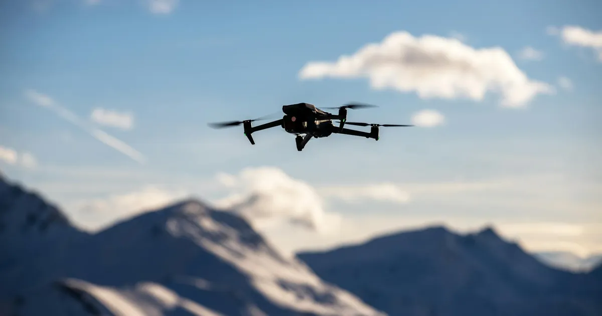 A drone flies over scenic snow-covered peaks under a clear blue sky, capturing breathtaking landscapes.