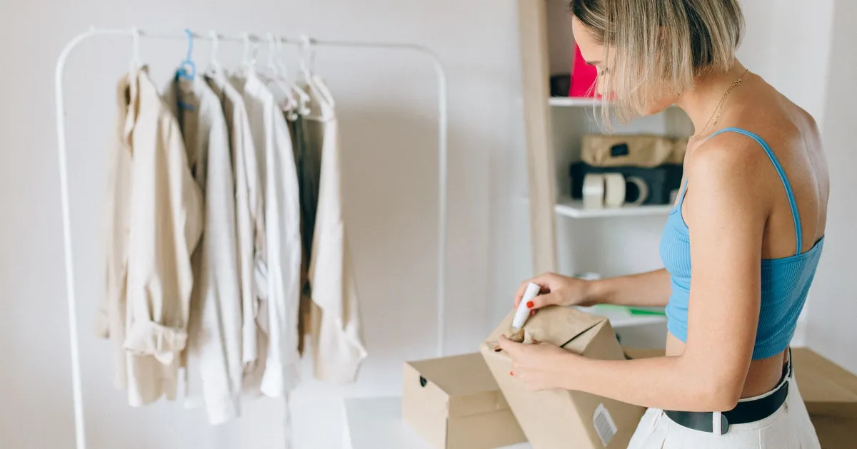 A woman in a blue top packs clothes into a box in a bright room.