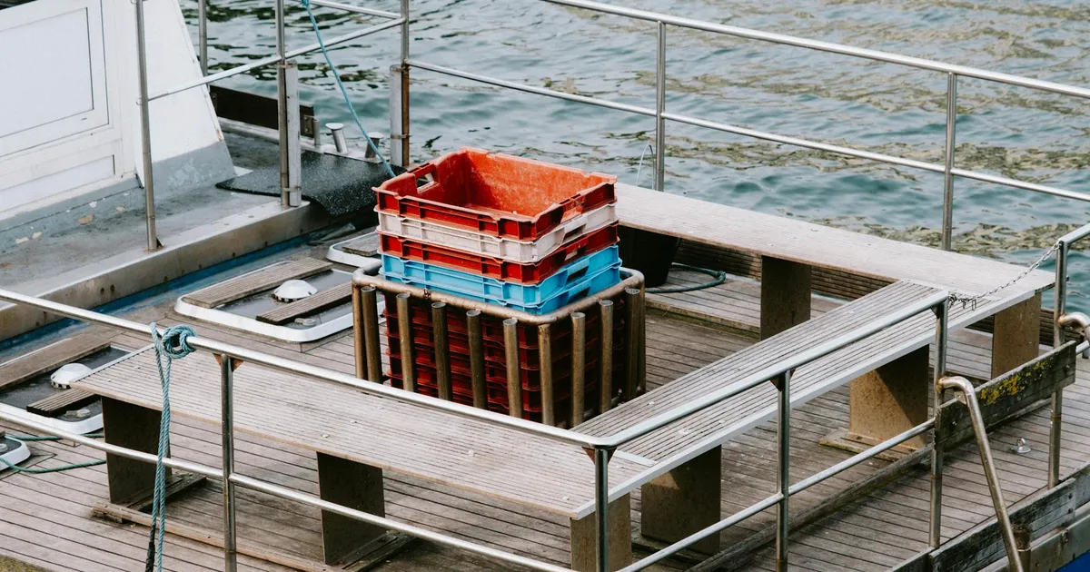 Close-up view of an empty fishing boat's wooden deck with stacked colorful crates and a calm water background.