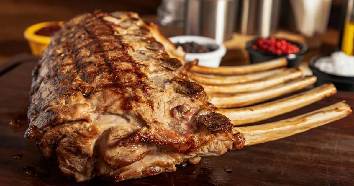 Close-up of seasoned grilled rack of lamb ribs on a rustic wooden board, perfect for gourmet dining.
