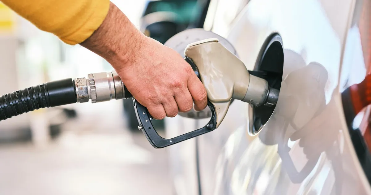 Close-up of a person refueling a car with a gas nozzle at a station.