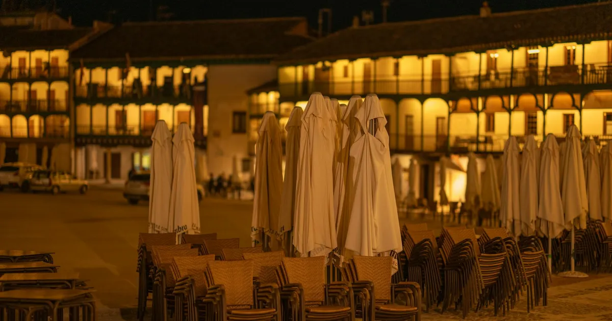Night view of the historic Plaza Mayor in Chinchón, Spain with stacked chairs and closed umbrellas.