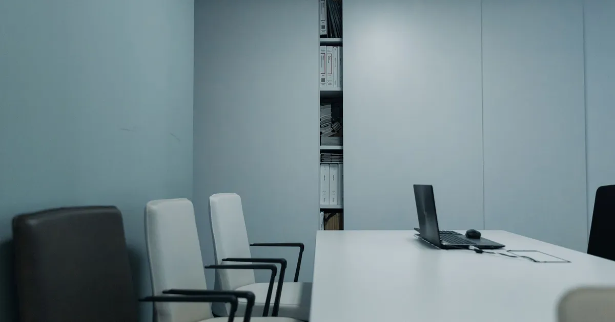 A sleek conference room with a white table and chairs, featuring a laptop on the table.