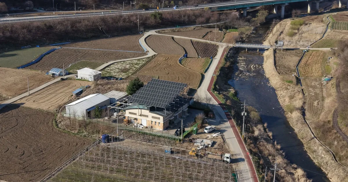 Aerial perspective of rural farmland featuring solar panels, fields, and a river.