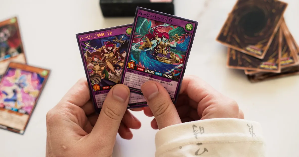 Hands holding Yu-Gi-Oh! trading cards in a dynamic gaming setup with blurred background.