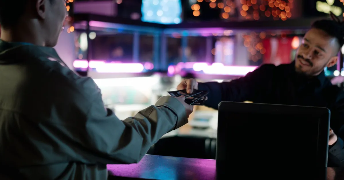 Man smiling while handing over and receiving tickets at a kiosk counter.