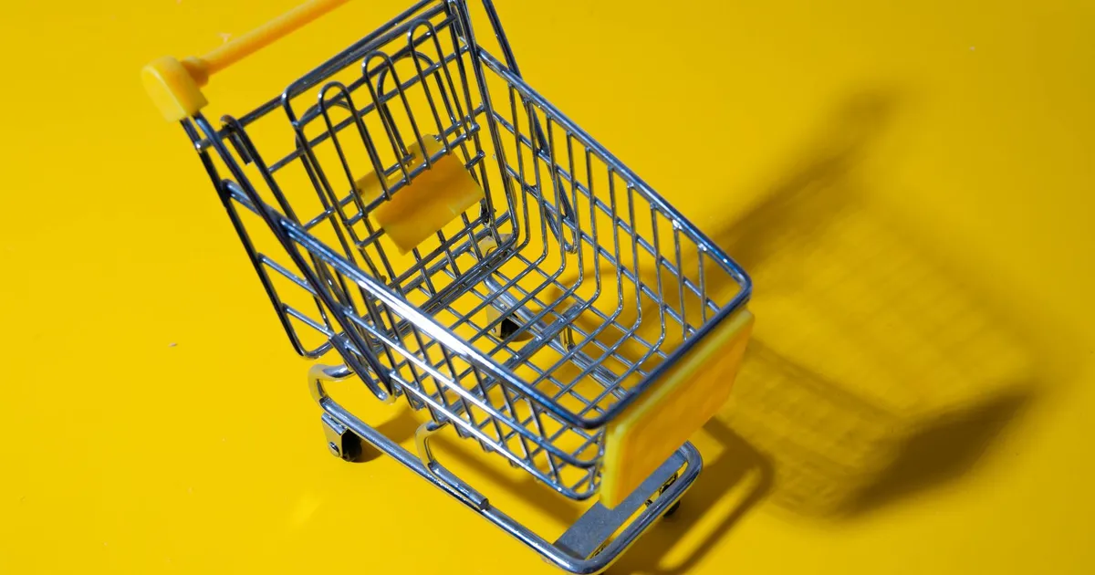 A toy shopping cart displayed against a vivid yellow background, casting a shadow.