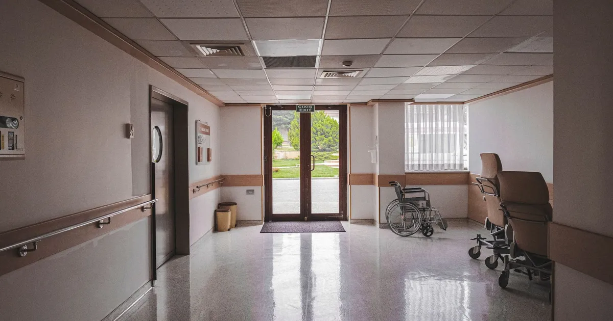 Hospital corridor with wheelchair, reflecting glass doors, and outdoor view. Ideal for healthcare themes.