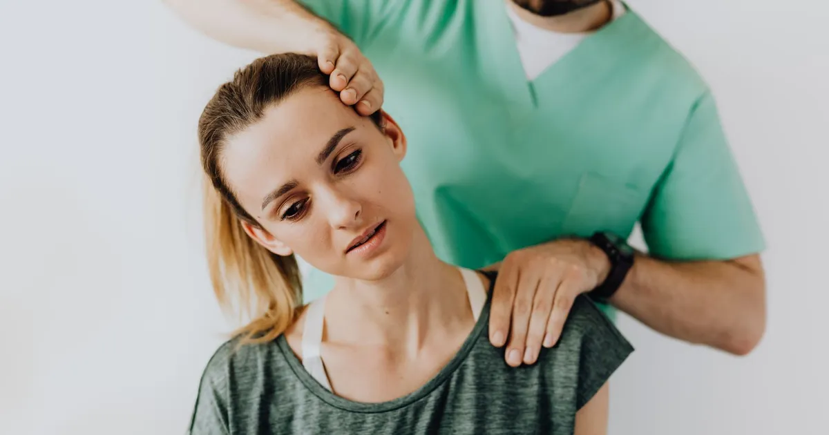 Positive male massage therapist gently massaging female patients neck and shoulders while stretching neck muscles