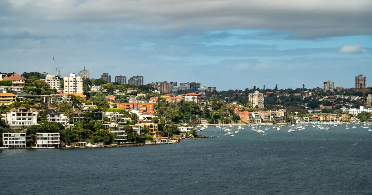 Scenic view of Sydney's harbour with boats and waterfront residences under a cloudy sky.
