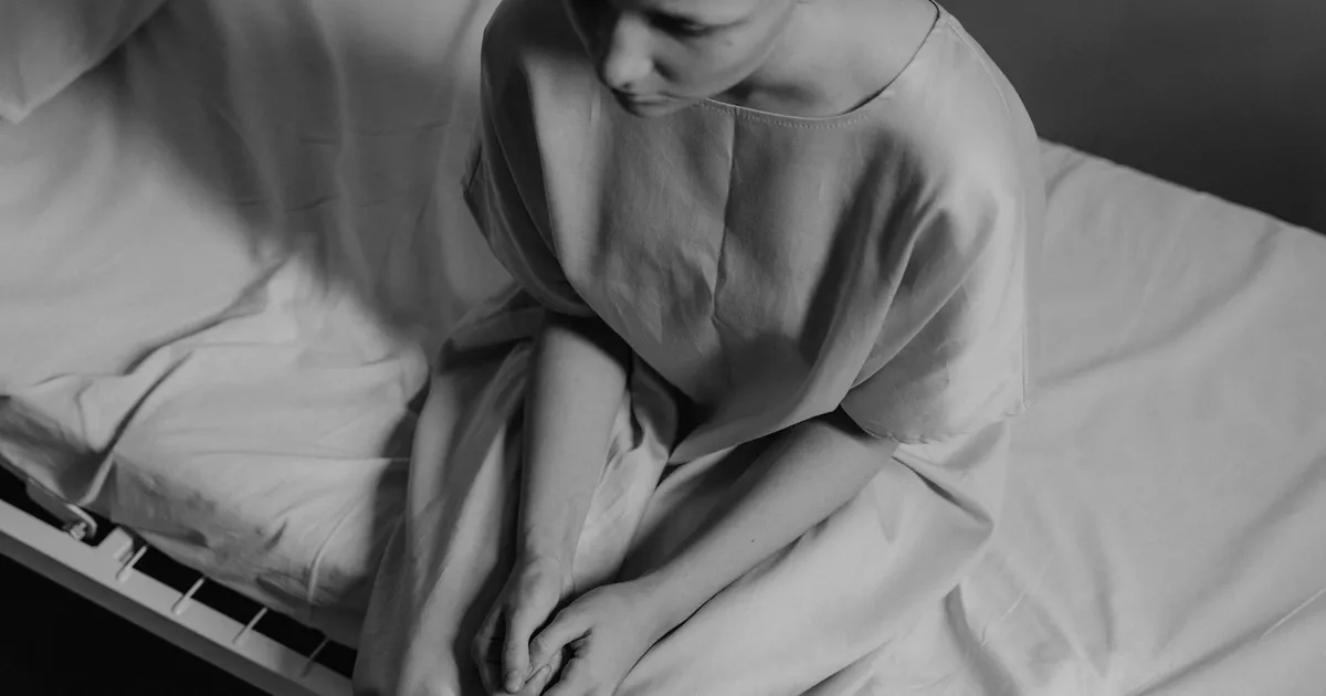 A poignant black and white photograph of a woman in a hospital setting, expressing vulnerability.