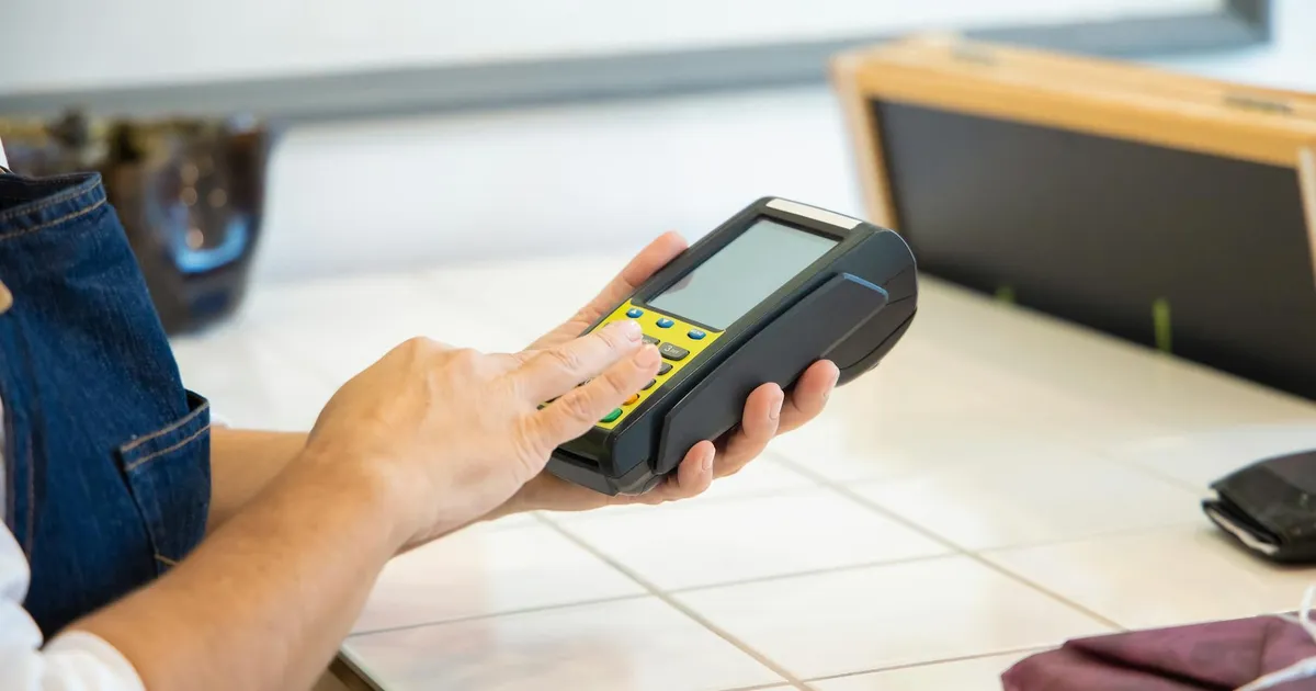 Close-up of hands using a POS machine in a retail setting, emphasizing digital payment.