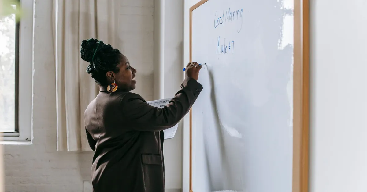 Side view of smiling African American woman writing on whiteboard standing in modern school classroom