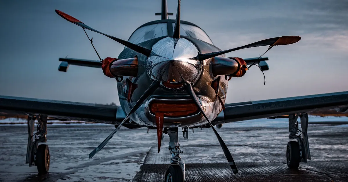 Detailed front view of a small aircraft with metallic shine, parked on the tarmac at dawn.