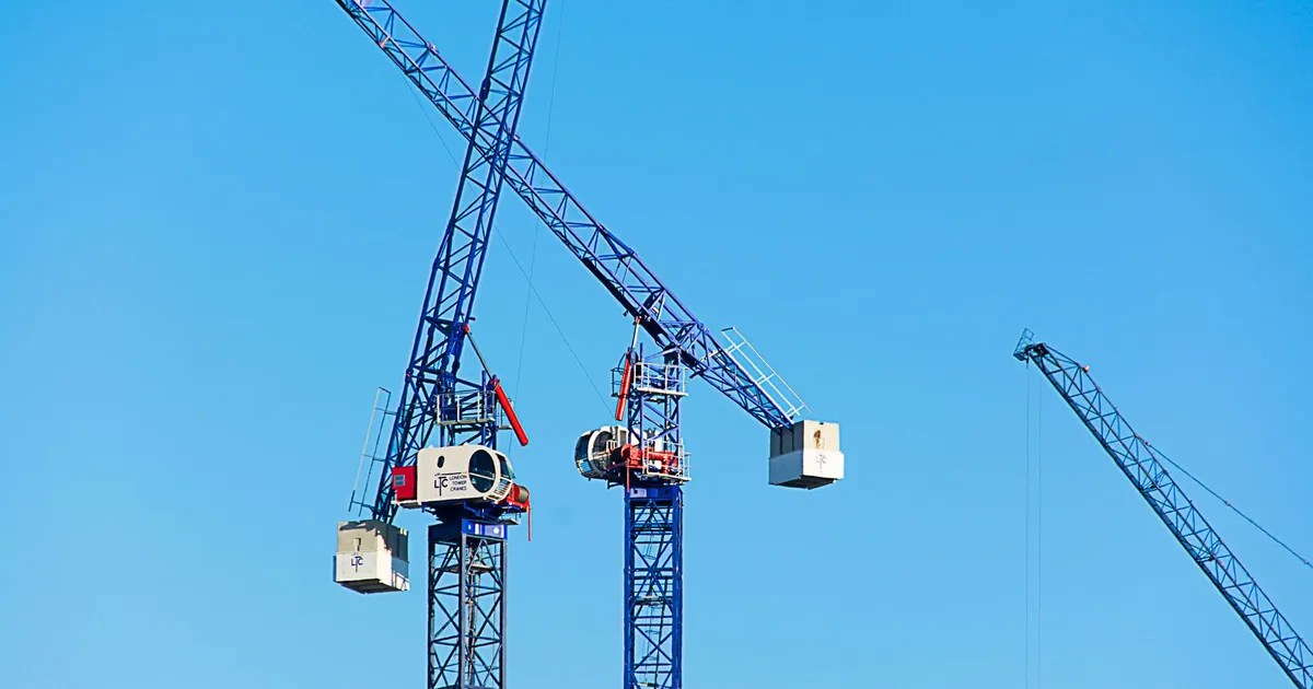 High vantage view of modern tower cranes operating under a clear blue sky on a construction site.