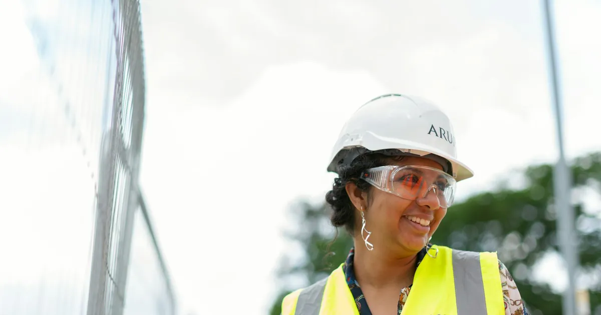 Smiling female engineer in protective gear at an outdoor construction site.
