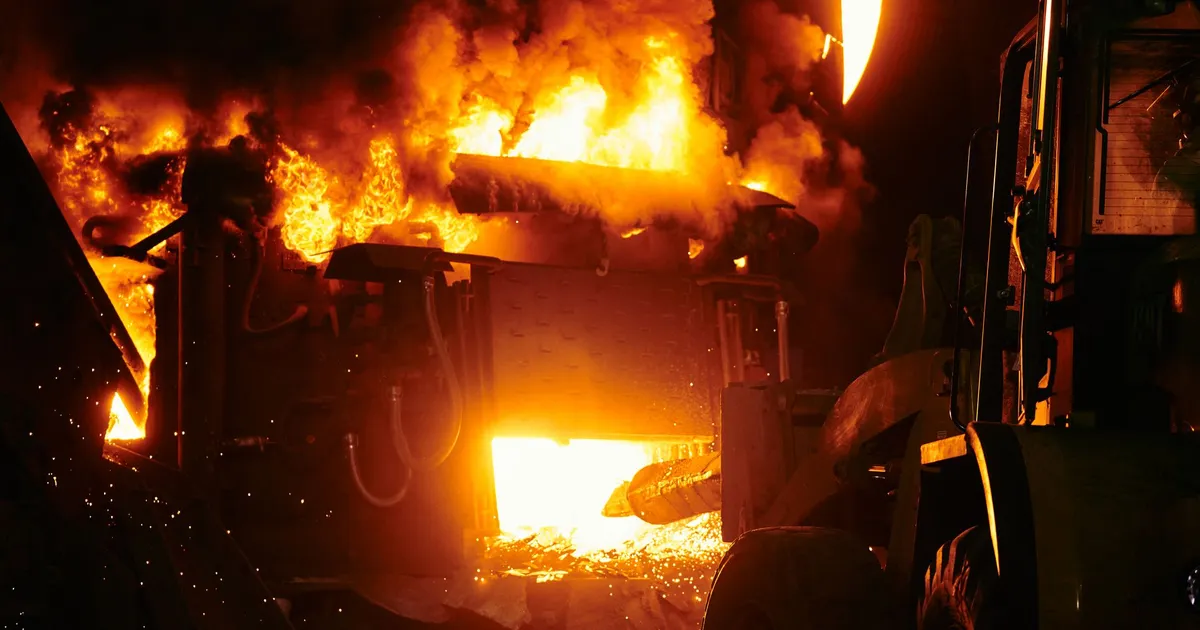 Dramatic image of an industrial furnace with bright flames and heavy machinery at night.