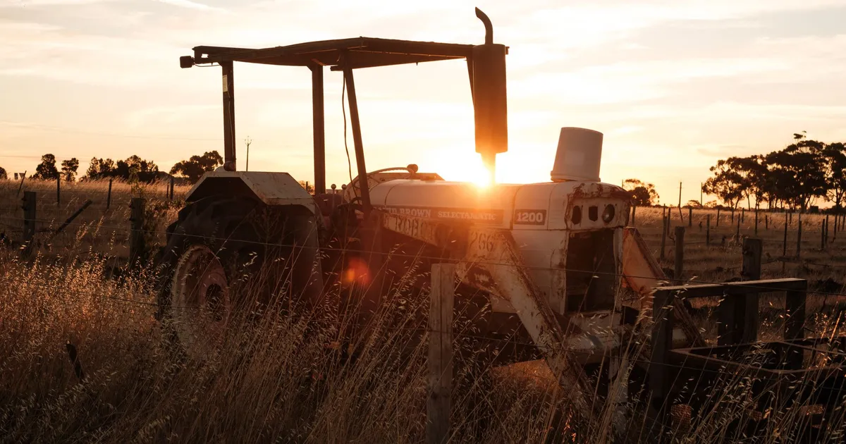 Rustic tractor silhouetted against a golden sunset in a rural field.