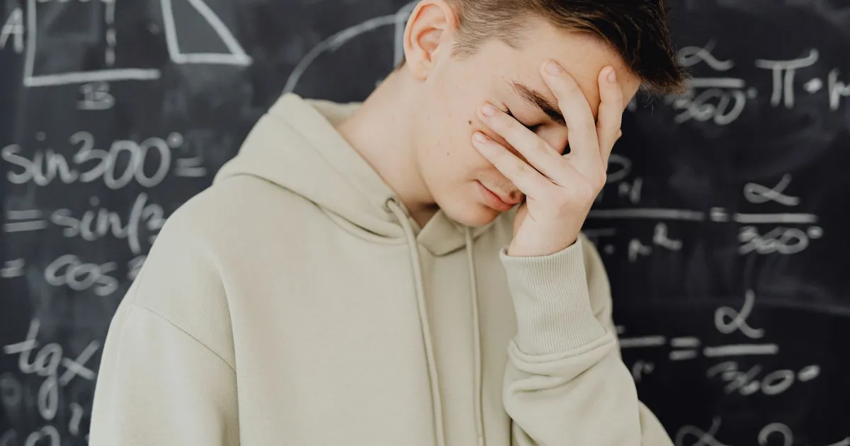 Young man overwhelmed by mathematical calculations on a blackboard in a classroom setting.