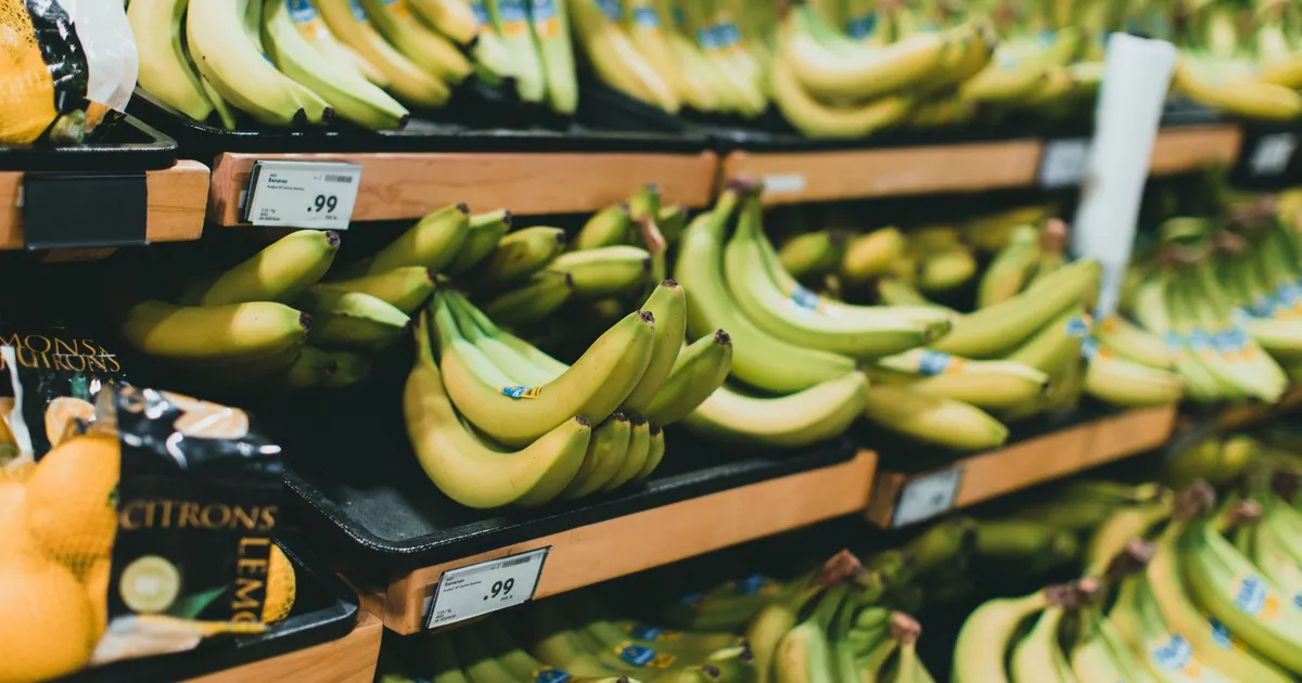 Close-up of fresh bananas stacked on grocery store shelves with price tags visible.
