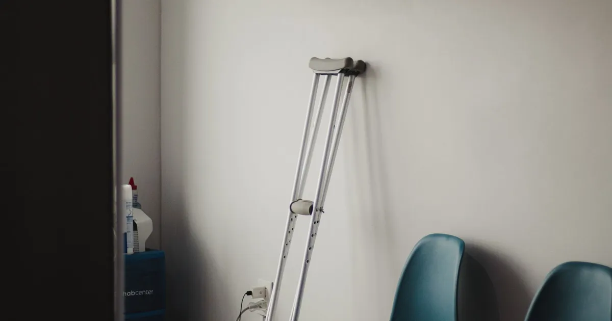 Crutches resting against a wall in a minimalist waiting room with blue chairs.