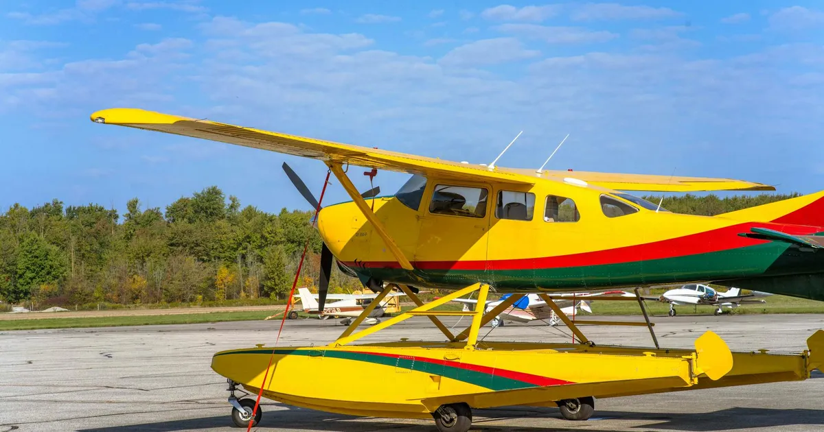 Bright yellow seaplane stationed outdoors at Stratford Airport in Ontario, Canada under clear blue skies.