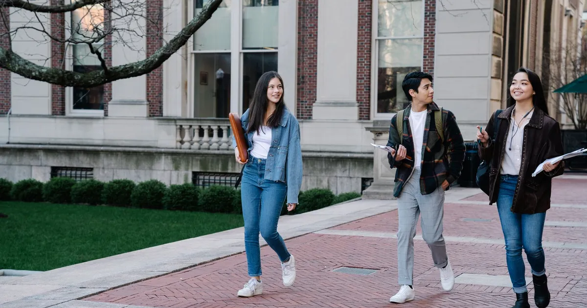 Group of young students walking on campus sidewalk on a bright day, showcasing casual university life.