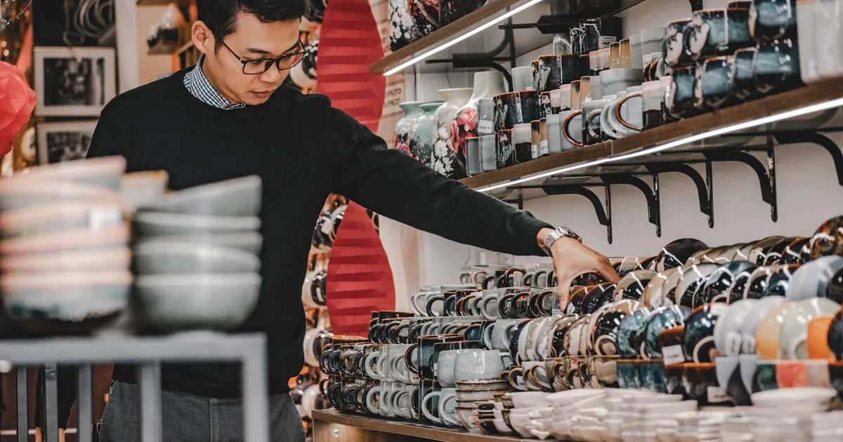 A man browsing a variety of ceramic mugs and bowls inside a shop in Hanoi, Vietnam.