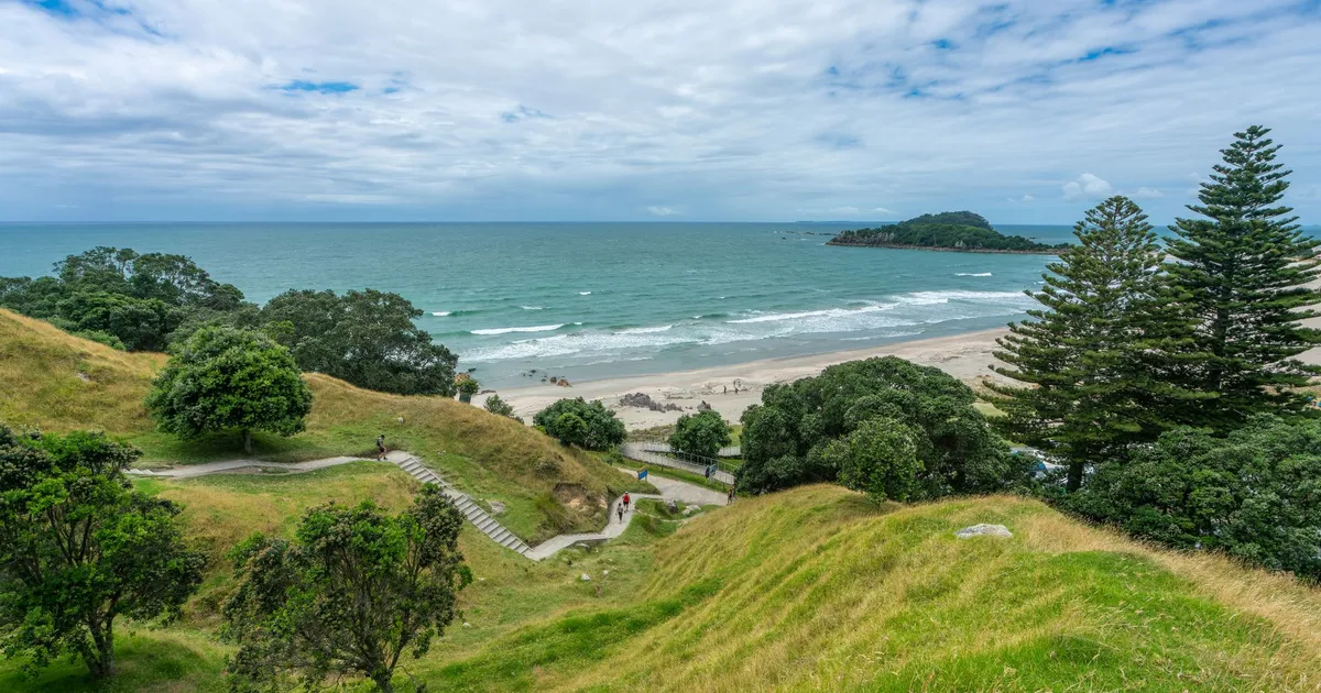 Breathtaking coastal landscape of Mount Maunganui, showcasing lush green hills, sandy shores, and vibrant blue sea.