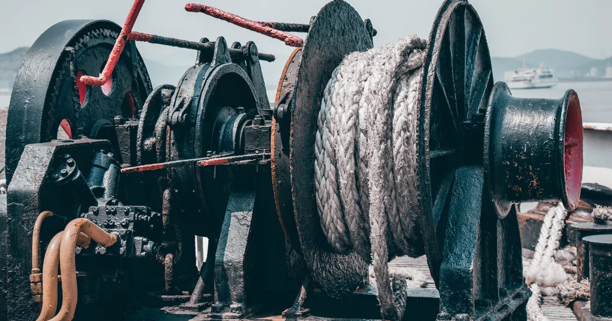 A close-up view of an industrial hydraulic winch on a ship deck with ropes.