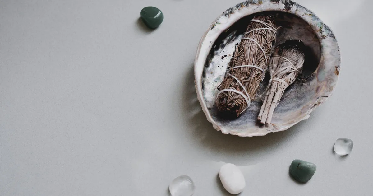 Flat lay of sage bundles and gemstones in an abalone shell for spiritual rituals.