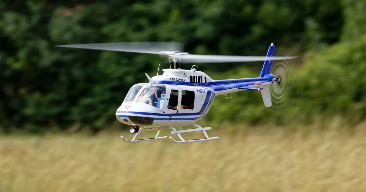 A police helicopter in flight over a lush green field, showcasing aviation technology.