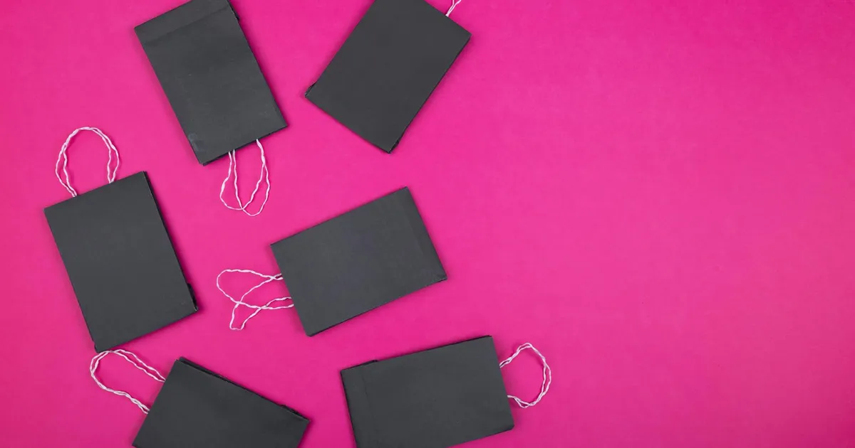 Flat lay of black paper bags arranged on a bright pink background, perfect for shopping concept visuals.