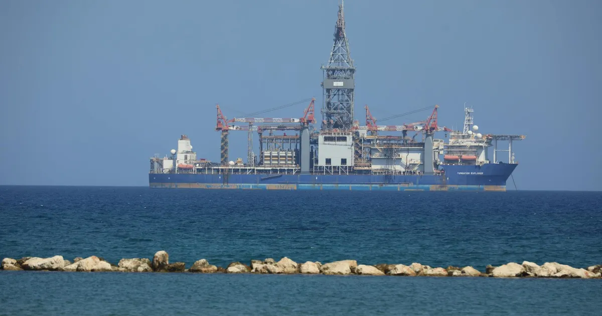 An offshore drilling rig floats on a calm sea with a clear blue sky in the background.