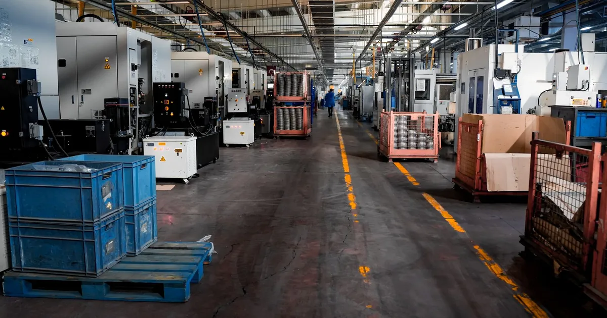 Vast industrial factory floor with machinery, crates, and structured workstations.