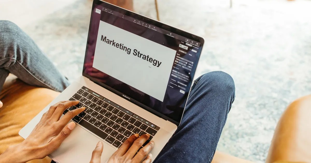 Close-up of hands using a laptop displaying a marketing strategy presentation indoors.
