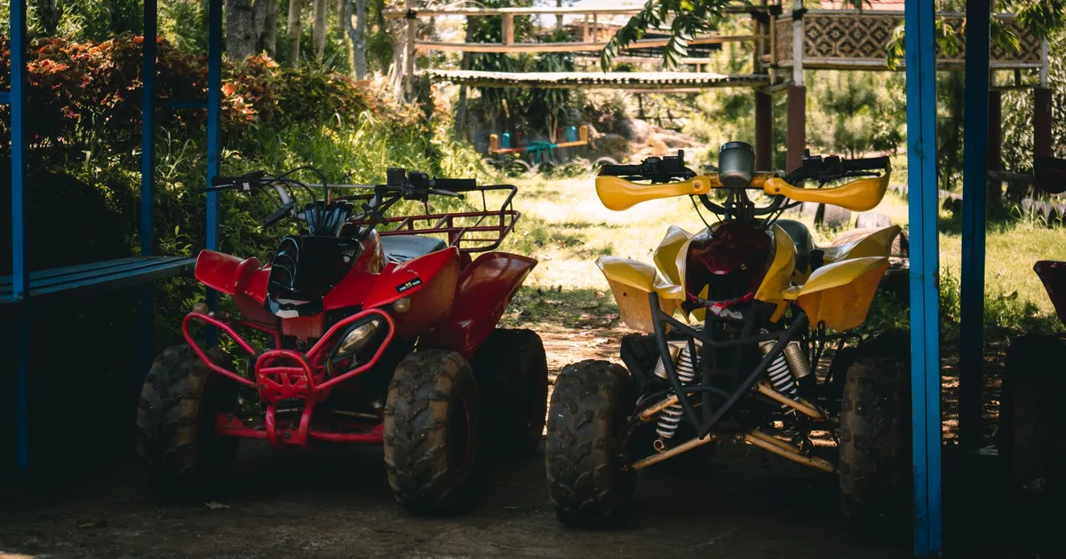 Two quad bikes parked under a shaded area surrounded by lush greenery.