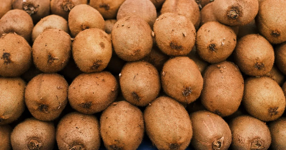 Cluster of fresh kiwi fruits stacked on a blue surface at a local market.