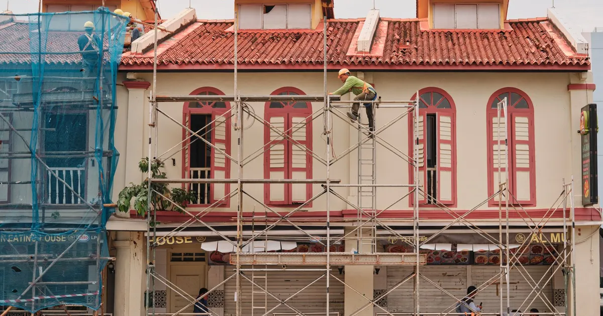 Workers on scaffolding renovating a historic building facade with red roof and tall windows.