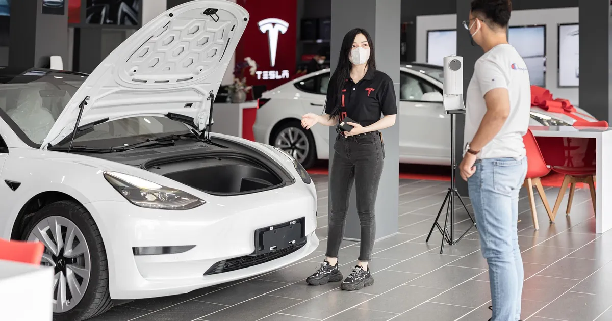 A customer talks with a sales representative about a Tesla Model 3 in a car dealership, showcasing the electric car's features.