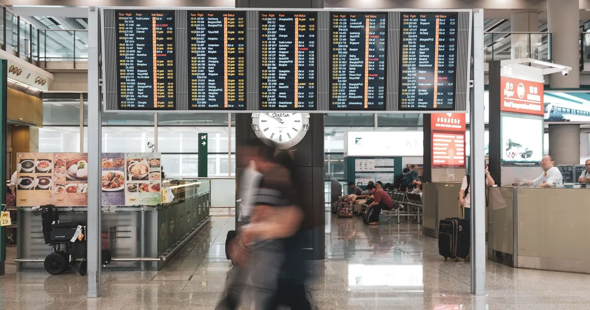 Blurred motion of travelers in a modern airport terminal with departure screens and a prominent clock.