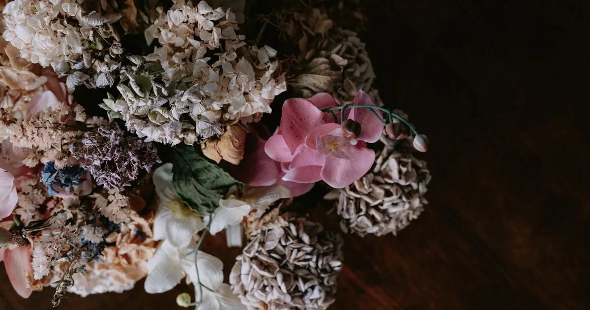 Artistic depiction of a withered bouquet featuring hydrangeas and orchids on a wooden surface.