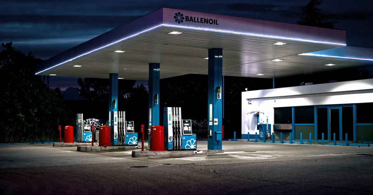 A brightly lit gas station under the night sky with an empty forecourt.