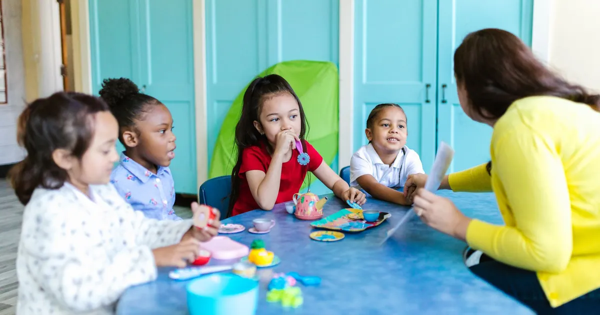 A group of preschoolers interacting with a teacher in a colorful classroom setting.