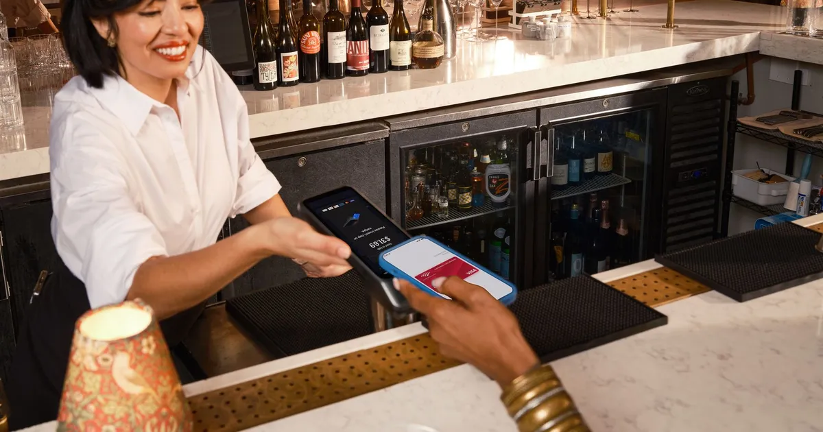A bartender assists a customer with contactless mobile payment at an upscale bar.